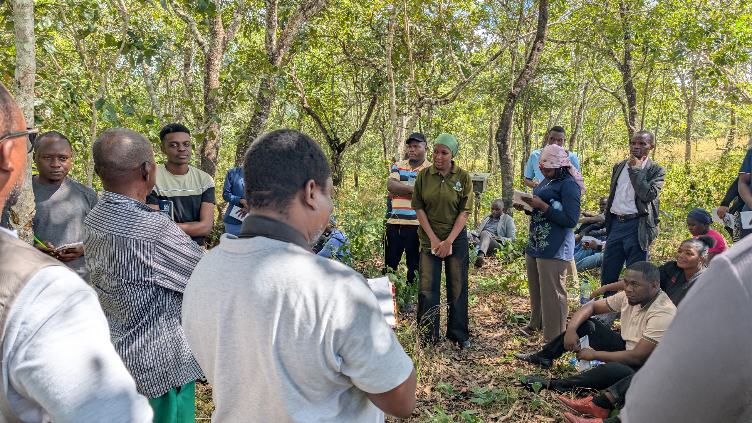 A large group of community members standing in a forest during a CONNECT Tanzania natural resource management training session