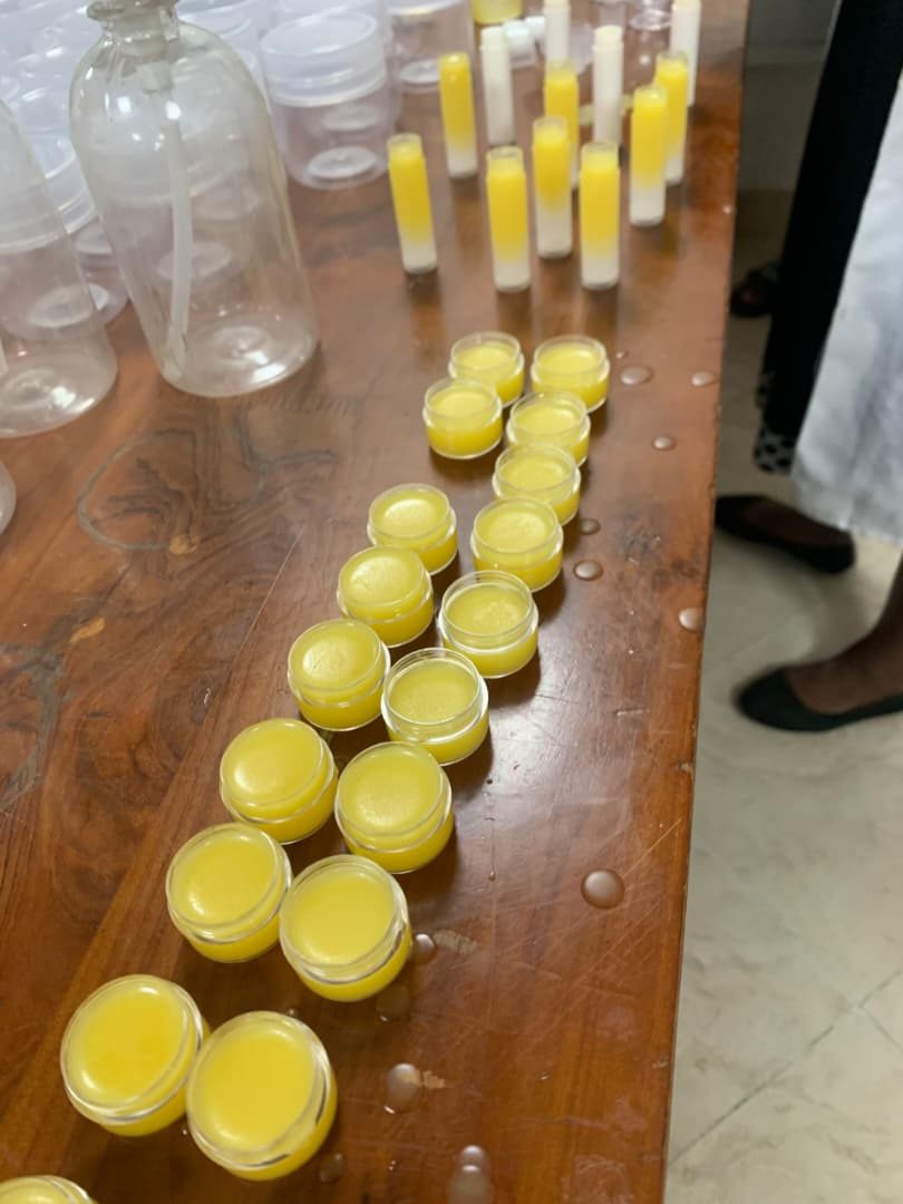 Clear jars and lip balm tubes filled with yellow beeswax products arranged on a wooden table